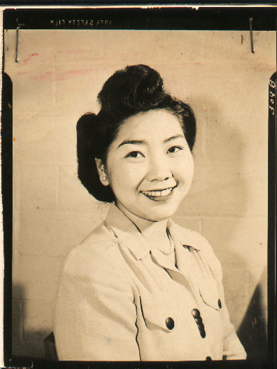 Portrait of Ellen Nakamura (née Noguchi) taken at Seabrook Farms in 1950. Ellen is wearing pearls and a button-up and smiling at the camera.