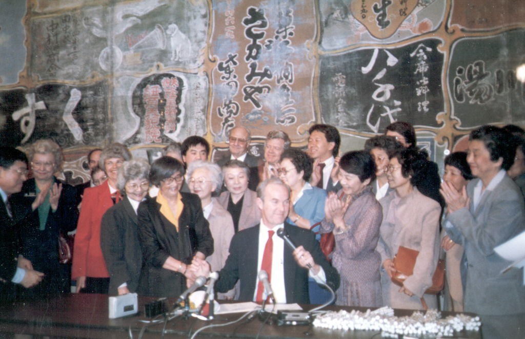 A large group of Nikkei clap as they watch a bill for redress payments being signed in front of them.