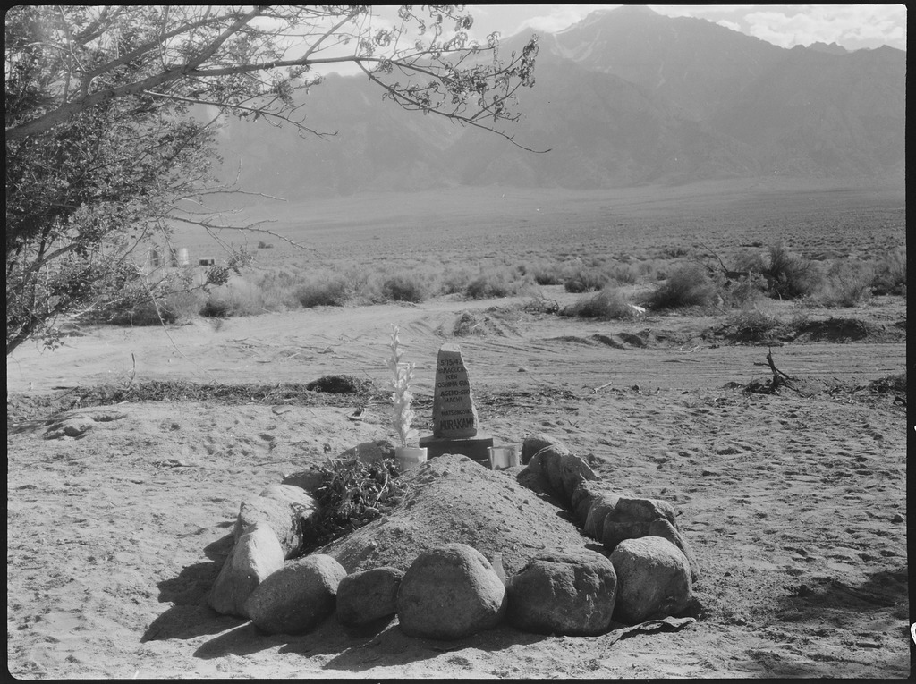 A black and white image of a grave at Manzanar. A large mound of dirt is surrounded by a circle of rocks.