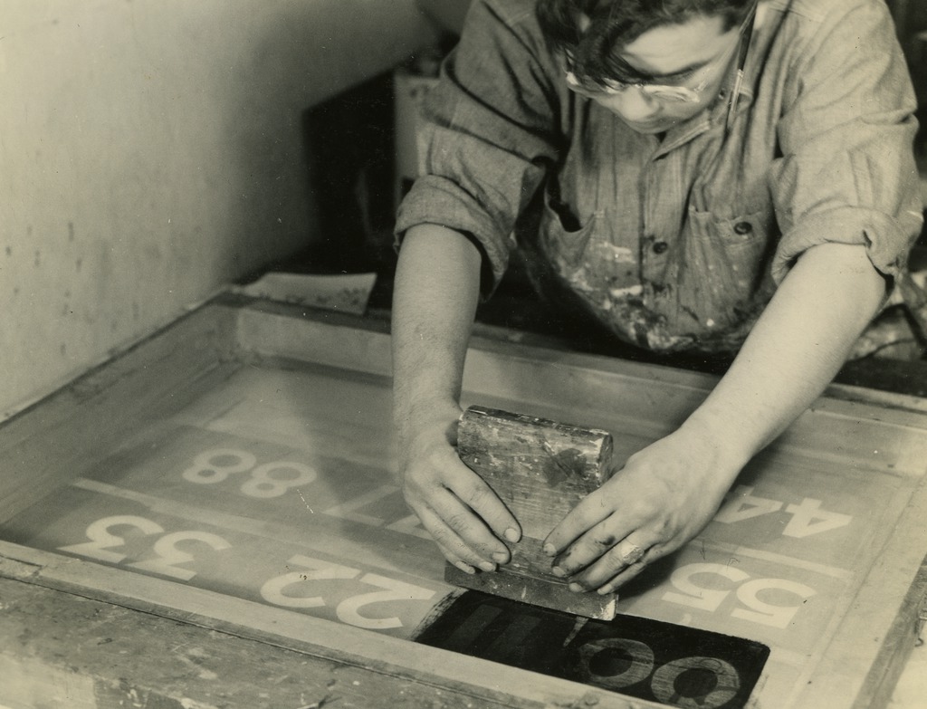 Black and white photo of a silk screen worker focused on printing numbers.