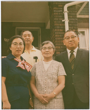 A Nikkei family stands in front of their home.