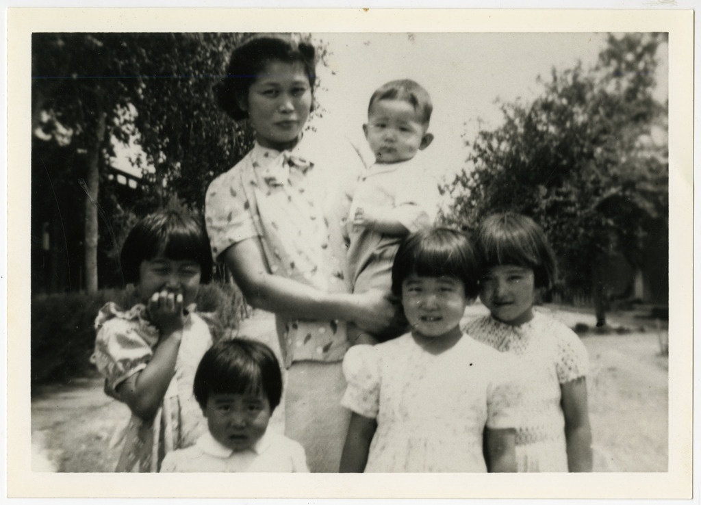 Black and white photo of Nikkei family. Standing in front of a tree lined road.
