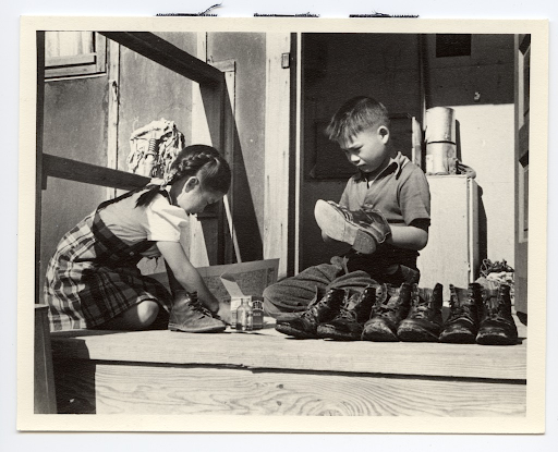 Two Japanese American children cleaning shoes on the front steps of a barrack in Heart Mountain.