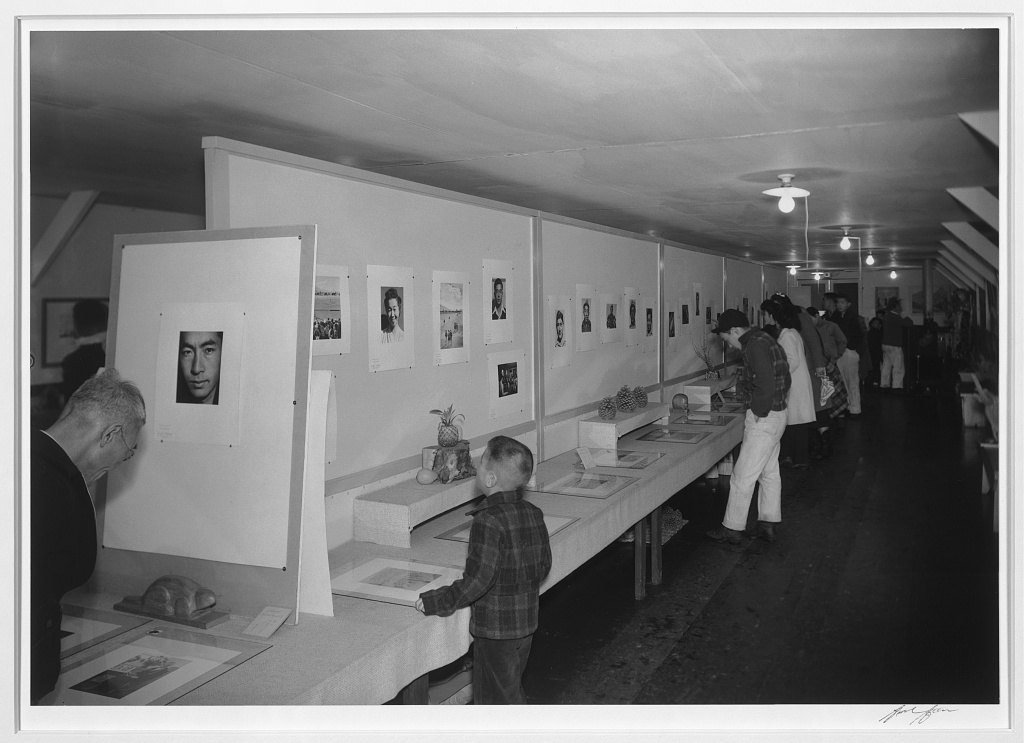 Japanese Americans of different ages looking at photos on display in an art exhibit at the Visual Education Museum inside Manzanar.